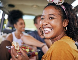 Woman smiling while eating meal with friends in car