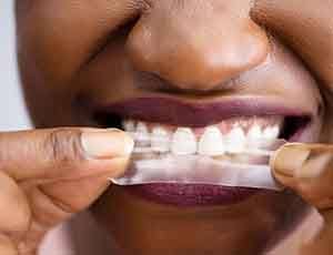 a woman placing a whitening strip on her teeth