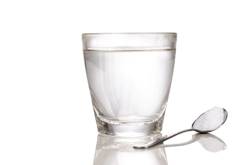 Glass of water next to spoonful of salt on reflective surface